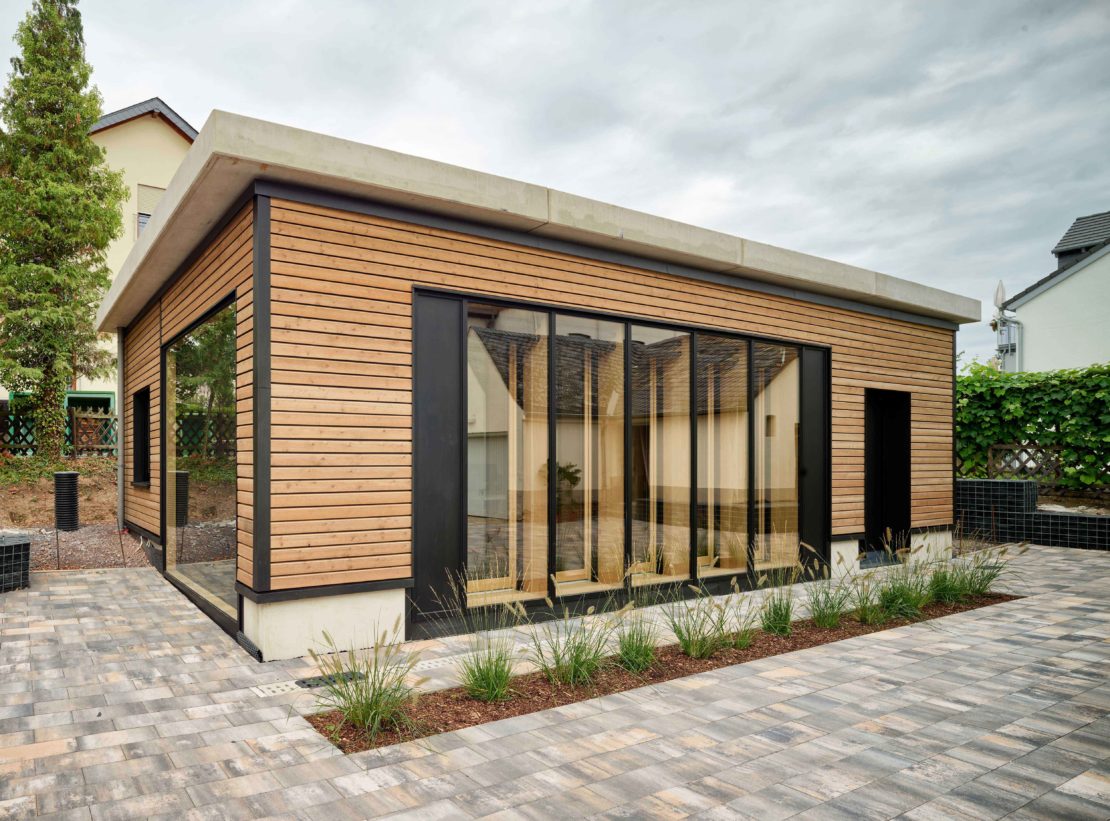 Auf dem Bild ist das energieautarke InnoLiving Gebäude in Kues zu sehen. Die Außenfassade, welche aus Holz-Betonverbundwänden besteht, wird gezeigt.