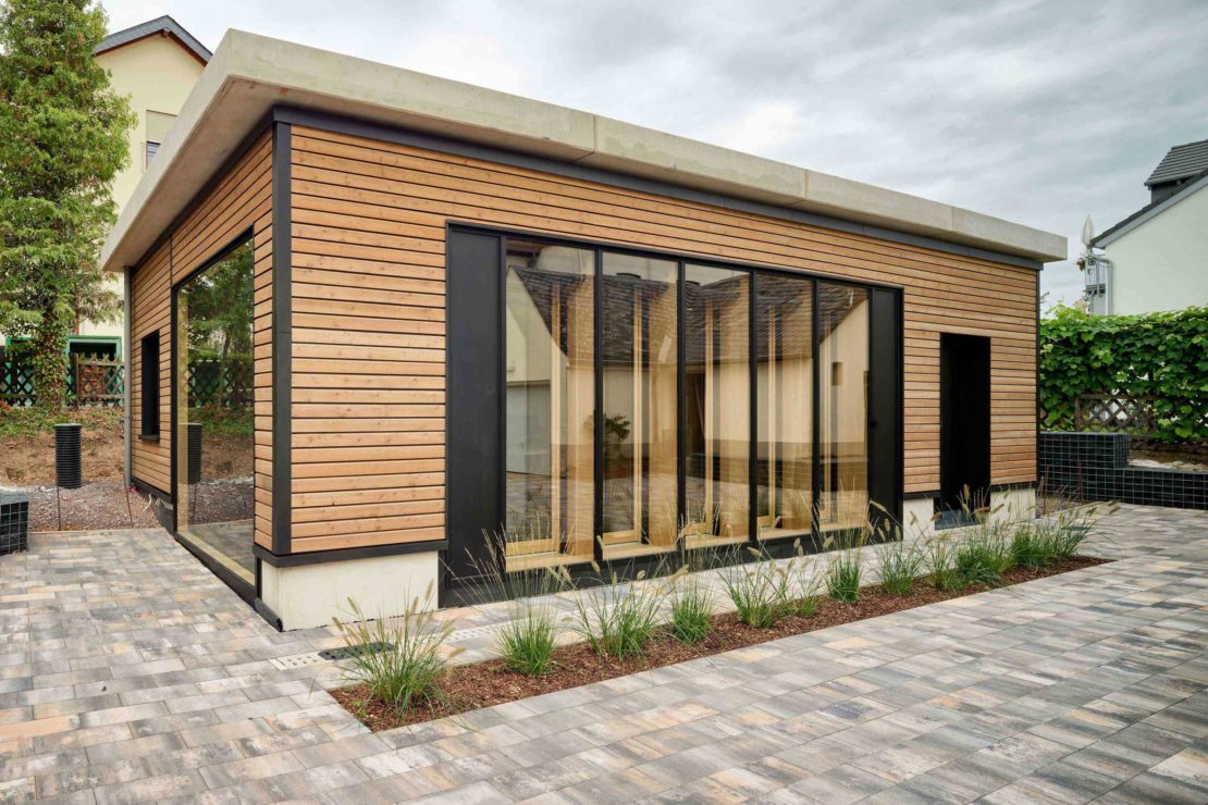 Auf dem Bild ist das energieautarke InnoLiving Gebäude in Kues zu sehen. Die Außenfassade, welche aus Holz-Betonverbundwänden besteht, wird gezeigt.